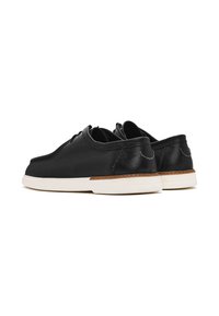 Chaussures en cuir noir avec bout arrondi, semelle en caoutchouc blanc et accents de couture marron sur le talon et l'entresemelle. Lacets à l'avant.