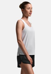 Hvid ærmeløs sportstop med løs pasform og rund halsudskæring, kombineret med sorte shorts med sideslidser for bedre bevægelsesfrihed.