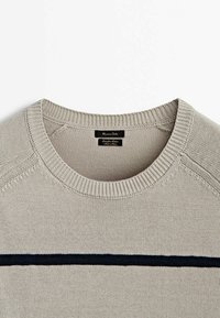 Beige gestrickter Pullover mit Rundhalsausschnitt, der einen dunklen horizontalen Streifen über der Brust und gerippte Bündchen sowie einen gerippten Saum aufweist. Etikett innen sichtbar.