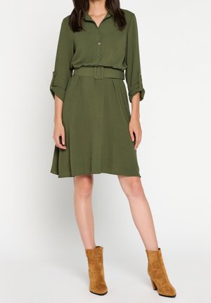 Oliwkowa sukienka koszulowa z paskiem w talii, zapięciem na guziki i podwiniętymi rękawami. Połączona z beżowymi zamszowymi botkami za kostkę.