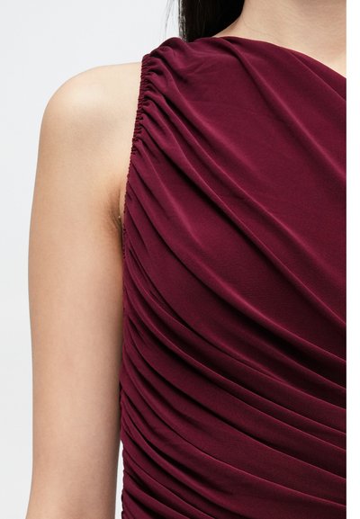 Borvörös ruha átlós redőzéssel, lágy textúrával és ujjatlan kialakítással, amely kiemeli a kecses redőket a felsőrész mentén.