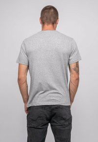 T-shirt gris à manches courtes en coton, avec un col rond classique et une texture lisse. Associé à un jeans sombre, affichant un design simple.