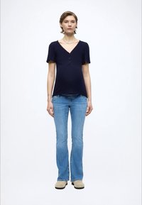 Top azul marino de manga corta con escote en V y dos botones, combinado con vaqueros acampanados azul claro y zapatos beige. Diseño sencillo y casual.