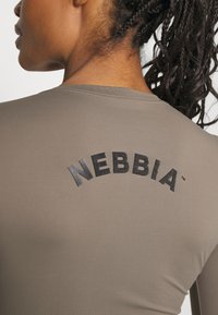 Dugi rukav majica u umirujućoj taupe boji s zakrivljenim crnim "NEBBIA" logotipom na leđima. Glatka tekstura s minimalnim detaljima šivanja.