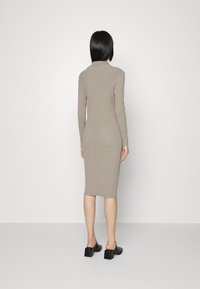 Vestido de malha canelada em cinza claro, com mangas longas, silhueta ajustada, altura até ao joelho, fenda lateral na barra, combinado com mules de salto bloco pretos.