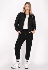 Sort cropped jakke med camouflage mønster, hvid tætsiddende top, sorte jogger bukser, og sort-hvide sneakers med stribede sokker.