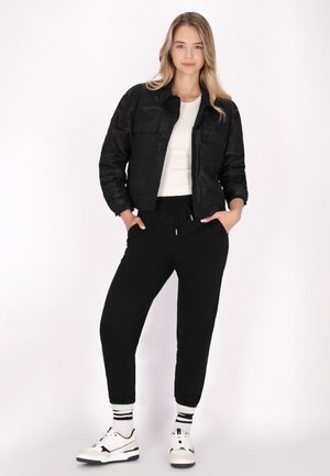 Sort cropped jakke med camouflage mønster, hvid tætsiddende top, sorte jogger bukser, og sort-hvide sneakers med stribede sokker.