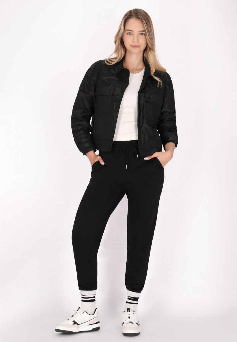 Sort cropped jakke med camouflage mønster, hvid tætsiddende top, sorte jogger bukser, og sort-hvide sneakers med stribede sokker.