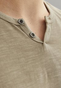 Khaki kortærmet henley skjorte med en tekstureret overflade, der har en to-knaps placket og en rund halsudskæring.