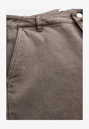 Lähikuva ruskeasta denim-kankaasta, jossa näkyy tasku, vyölenkki ja hopeinen nappi housujen vyötäröllä.