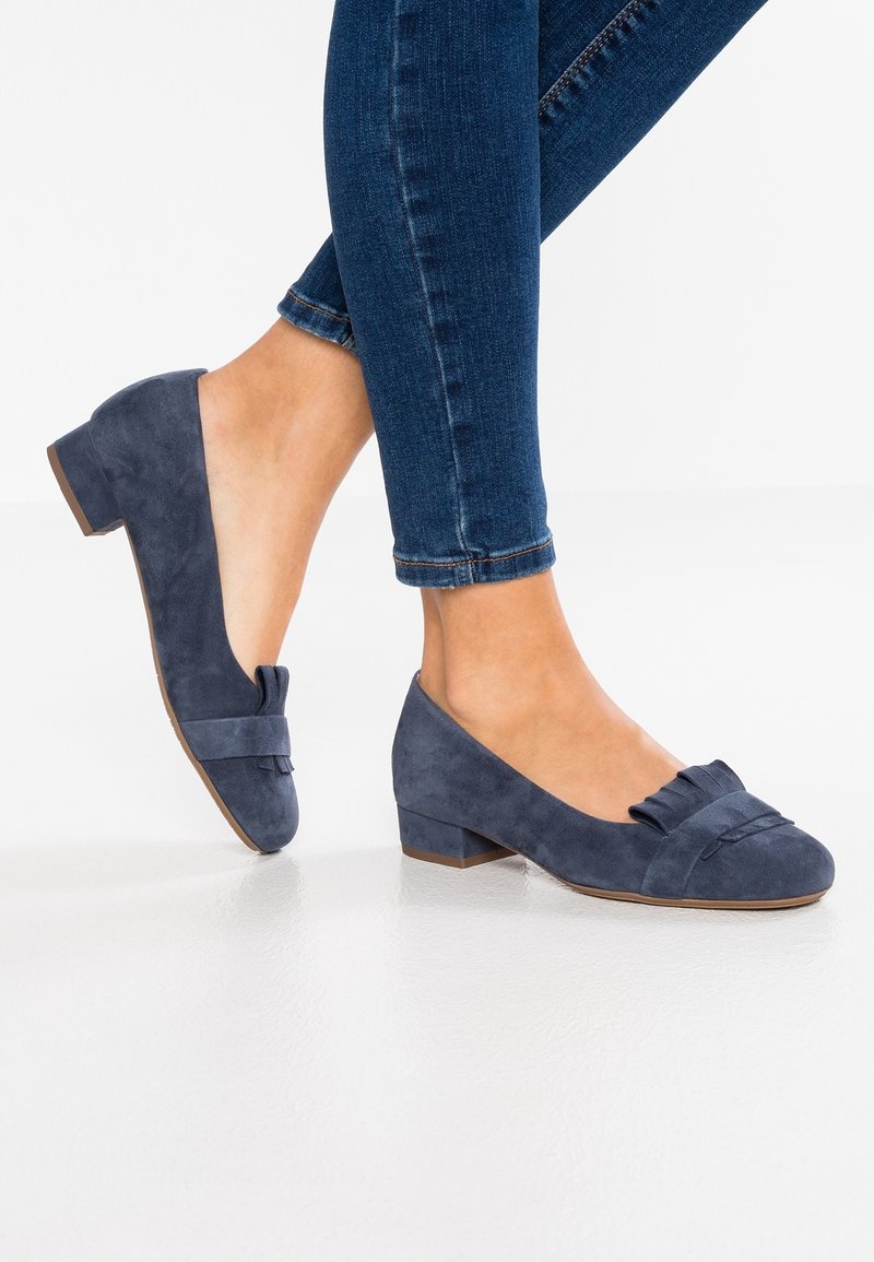Ballerine in suede blu navy con un piccolo tacco, caratterizzate da un fiocco decorativo sul davanti e una texture liscia. Indossate con jeans scuri aderenti.