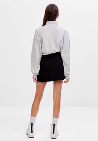 Felpa grigia corta con colletto alto e spalle ribassate, abbinata a una mini gonna nera plissettata e scarpe platform bianche.