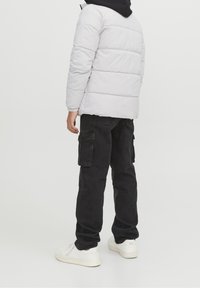 Biała, pikowana kurtka puchowa z kapturem, w połączeniu z czarnymi spodniami typu cargo i białymi sneakersami. Charakteryzuje się luźnym krojem i ściągaczami na mankietach.