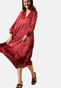 Robe en satin rouge avec des manches longues, décolleté en V, buste à volants, ourlet en dentelle, et coupe décontractée, associée à des sandales marron.