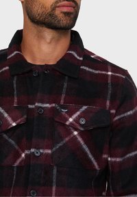 Ruutukuosiset flanellipaita burgundin, mustan ja valkoisen väriyhdistelmässä. Siinä on napitettu rintatasku ja kaulus. Pehmeä rakenne ja klassinen ruudullinen malli.