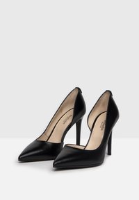 Escarpins noirs en cuir avec un bout pointu, un talon stiletto effilé et un design à dos ouvert, présentant une texture lisse et un minimum de détails.