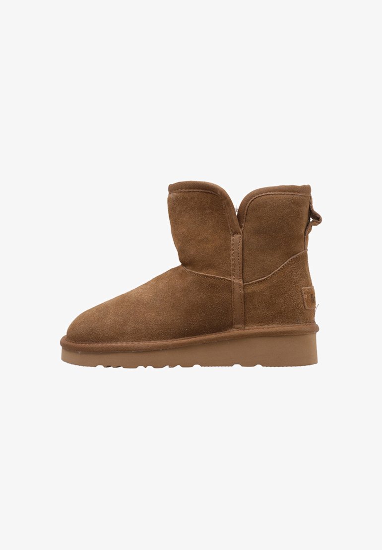 Botines de ante marrón con punta redondeada, caña corta y suela de goma plana. Incluyen una lengüeta trasera para facilitar su uso.