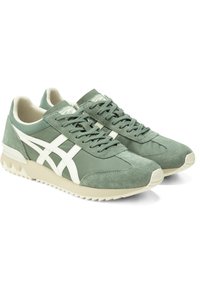 Green sneakers with suede and textile materials, featuring white side stripes, lace-up closure, and a textured rubber sole.