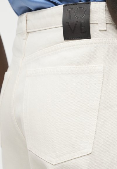 Približen posnetek zadnjega žepa belih kavbojk iz jeansa z oznako iz črnega usnja, na kateri je vgravirana beseda "LOVE", na pasu.