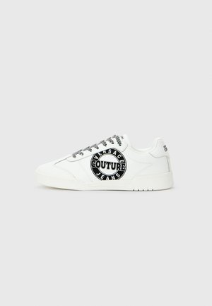 Sapatilha baixa branca com atacadores preto e branco e grande logotipo circular preto "Versace Jeans Couture" na lateral.