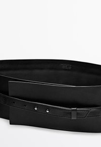 Czarny skórzany pasek z wąską klamerką, prezentujący gładką fakturę i wiele otworów do regulacji, położony na białej powierzchni.