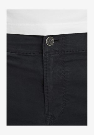 Czarne bawełniane spodnie mają płaski przód z metalowym guzikiem i zapięciem na zamek. Widoczne szwy wzdłuż kieszeni i szwów.