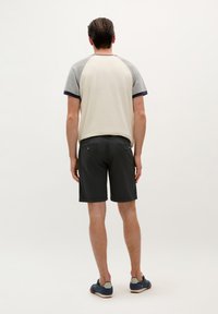 Conjunto casual masculino que incluye una camiseta de manga corta en color crema y gris con estilo raglán, combinada con pantalones cortos oscuros y zapatos azules. Diseño sencillo, con detalles mínimos.