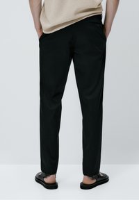 Mustat kevyet suoralahkeiset housut, joissa on sivutaskut, hienovarainen tekstuuri ja sileä viimeistely, yhdistetty mustiin sandaaleihin.