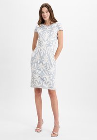 Blaues Kleid mit weißer Blumenstickerei, kurze Ärmel, knielang, Rundhalsausschnitt, Seitentaschen, kombiniert mit silbernen Riemchen-Ankle Boots.