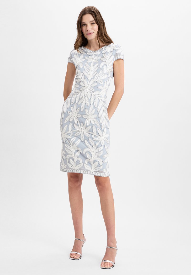 Blaues Kleid mit weißer Blumenstickerei, kurze Ärmel, knielang, Rundhalsausschnitt, Seitentaschen, kombiniert mit silbernen Riemchen-Ankle Boots.