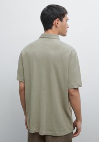Polo a maniche corte di colore verde oliva chiaro, realizzato in tessuto morbido. Presenta un colletto classico e una vestibilità rilassata, con orlo dritto.