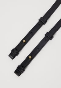 Zwarte leren riemen met gaten voor aanpassingen, voorzien van koperen studs en lusvormige uiteinden voor bevestiging. Glad oppervlak overal.