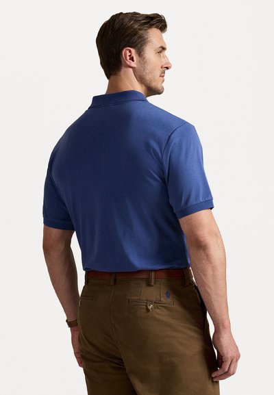 Cămașă polo cu mânecă scurtă pentru bărbați, de culoare albastră solidă, cu guler clasic și țesătură texturată, asortată cu pantaloni maronii și o curea din piele.