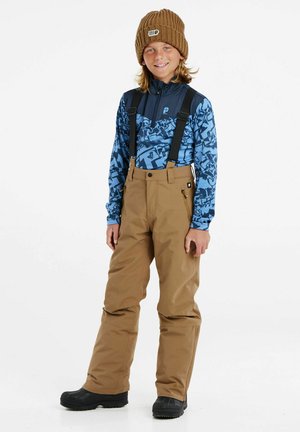 Haut à manches longues bleu avec un design géométrique, pantalon de neige beige avec bretelles, et un bonnet en tricot marron. Des bottes de neige noires complètent le look.