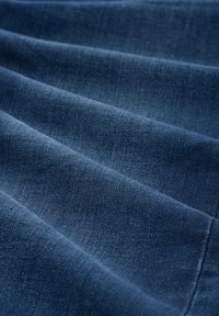 Gros plan sur un tissu en denim bleu foncé avec une texture en tissage diagonal et des plis doux créant des crêtes ombragées.