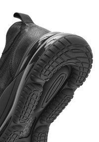 Zapatilla negra con parte superior de cuero texturizado, suela negra brillante y banda de goma con un patrón para mayor tracción. Se puede ver una lengüeta en la parte trasera.