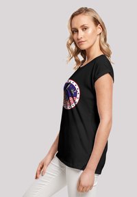 Black t-shirt with short sleeves featuring a circular graphic in blue, white, and red, depicting an eagle and stars, on a textured surface.