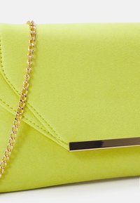 Sac pochette vert néon en texture douce avec un rabat, doté d'une bandoulière en chaîne dorée et d'une barre d'accent métallique à l'avant.