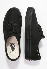 Baskets en toile noire à profil bas, bout rond, fermeture à lacets, semelle extérieure noire texturée et petit logo sur la semelle intérieure.