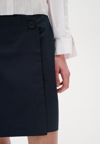 Granatowa spódnica dopasowana z płaskim przodem, z zapięciem na boczny guzik i gładką teksturą, połączona z białą koszulą z długim rękawem.