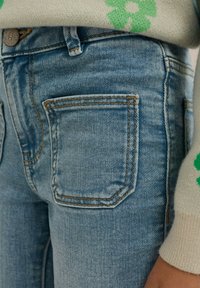 Ljusblå denimjeans har en standardficka med kontrasterande orange sömmar. Tyget har en något blekt textur, vilket ökar hållbarheten.