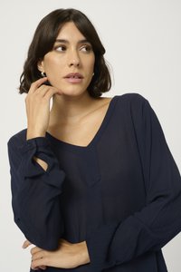 Top blu navy a maniche lunghe con scollatura a V e tessuto testurizzato. Presenta polsini con bottone e un fit rilassato.