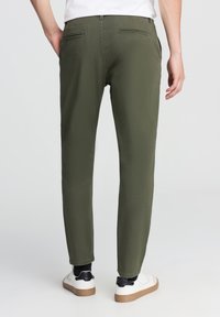 Khaki zielone spodnie w zwężanym kroju, wykonane z bawełny. Posiadają dwie tylne kieszenie i podwinięte nogawki, zestawione z białymi sneakersami.