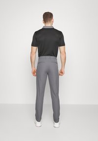 Black short-sleeve polo shirt paired with gray trousers. Trousers feature a smooth texture and back pockets. The model is viewed from behind.