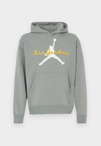 Sweat à capuche gris avec poche avant, présentant une silhouette blanche de Jumpman de basket-ball et un texte jaune "air jordan" sur la poitrine.