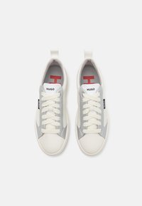 Białe i szare sneakersy o gładkiej teksturze, z wiązaniem i detalem logo na języku. Posiadają kontrastującą gumową podeszwę.