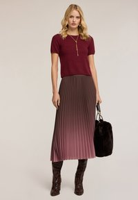 Burgundská krátká svetr s krátkým rukávem v kombinaci s plisovanou midi sukní, přecházející z mauve do tmavě fialové. Oblečeno s tmavými, lesklými botami s hadím vzorem.