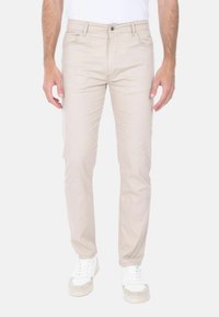 Pantaloni in cotone beige slim fit, dotati di tasche anteriori, chiusura con zip e bottone. Abbinati a sneakers bianche.