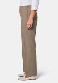 Beige, rechte broek met een elastische tailleband en zijnaad. Gepaard met witte instappers. Zachte, gestructureerde stof, minimale details.