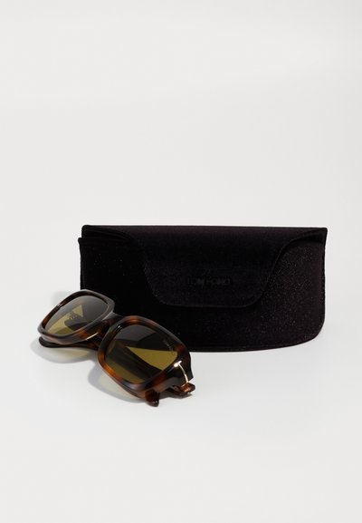 Braune Schildplatt-Sonnenbrille mit grünen Gläsern, die ein klobiges rechteckiges Design aufweist. Begleitet von einem schwarzen Samt-Etui.